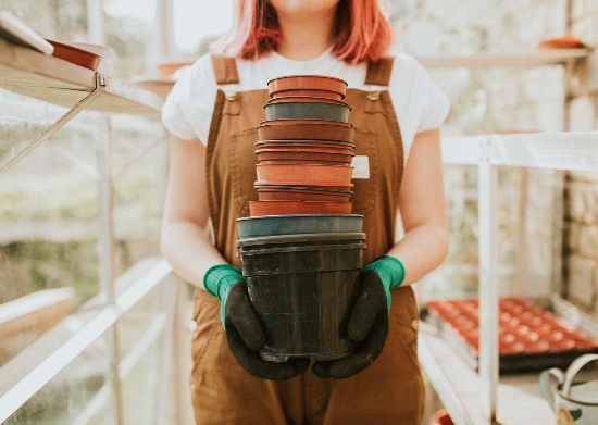 A photo of a woman in a greenhouse holding a stack of empty plant pots